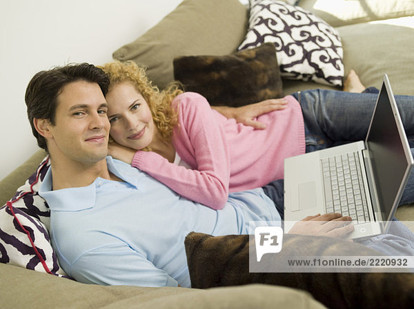 Young couple on sofa using laptop  smiling