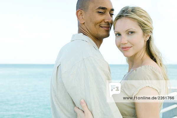Couple embracing  both smiling at camera  ocean in background