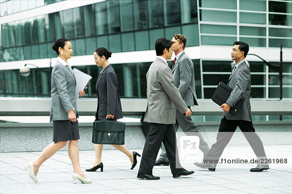 Male and female professionals walking on busy sidewalk  side view