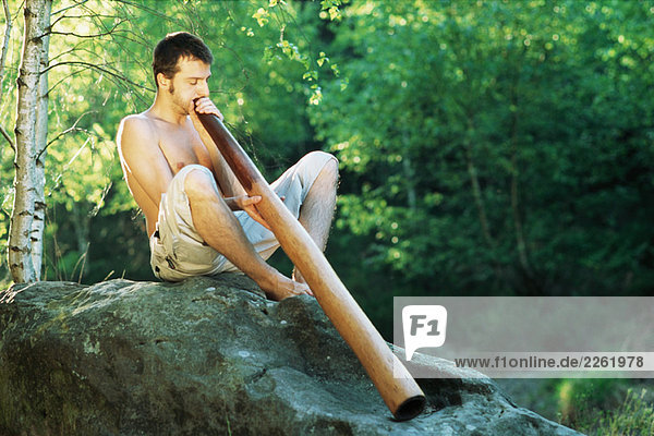 Mann im Freien sitzend  Didgeridoo spielend  Augen geschlossen