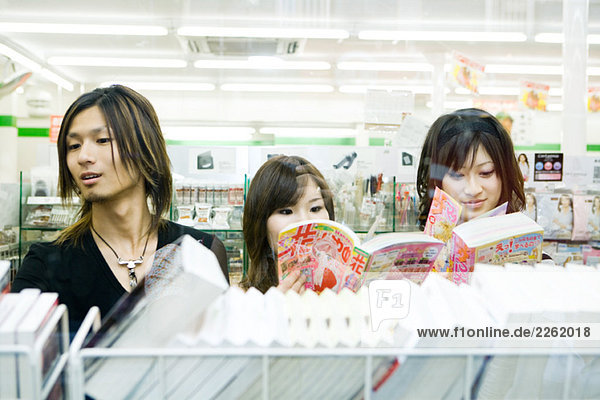 Drei junge Freunde Seite an Seite im Geschäft  die sich Comics im Manga-Stil ansehen.