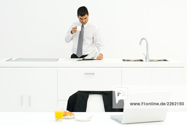 Geschäftsmann in der Küche stehend  Zeitung lesen und Kaffee trinken  Frühstück auf dem Tisch im Vordergrund