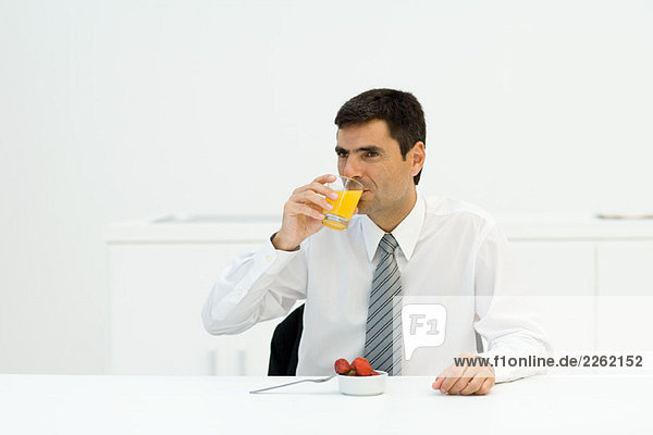 Geschäftsmann am Tisch sitzend  Orangensaft trinkend  wegschauend