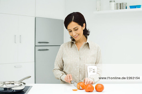 Frau steht an der Küchentheke  schneidet Tomaten mit Messer auf