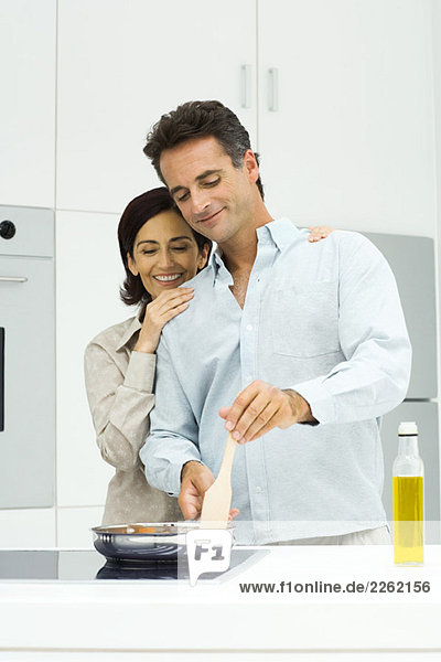 Couple cooking together in kitchen  woman leaning head on man's shoulder  both looking down