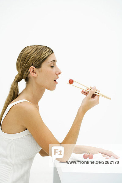 Frau isst rote Traube mit Stäbchen  Augen geschlossen  Seitenansicht