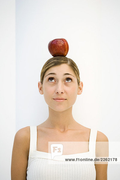 Junge Frau mit ausgewogenem Apfel auf dem Kopf  aufblickend  Portrait