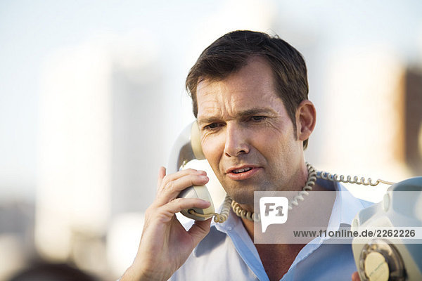 Man talking on landline phone  cord wrapped around his neck  close-up