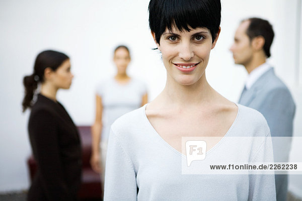 Junge Geschäftsfrau lächelt vor der Kamera  Kollegen stehen im Hintergrund