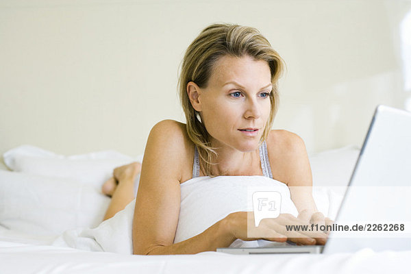 Frau auf dem Bett liegend  mit Laptop-Computer  wegschauend