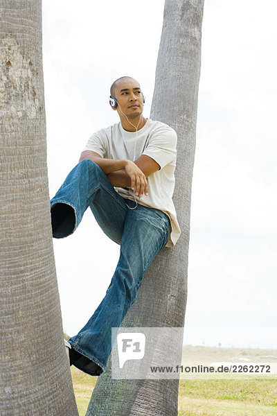 Man sitting on tree trunk  listening to headphones  looking away