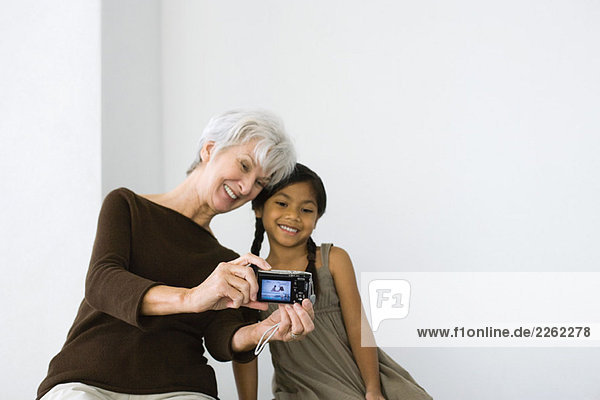 Senior woman photographing self and granddaughter with digital camera  both smiling