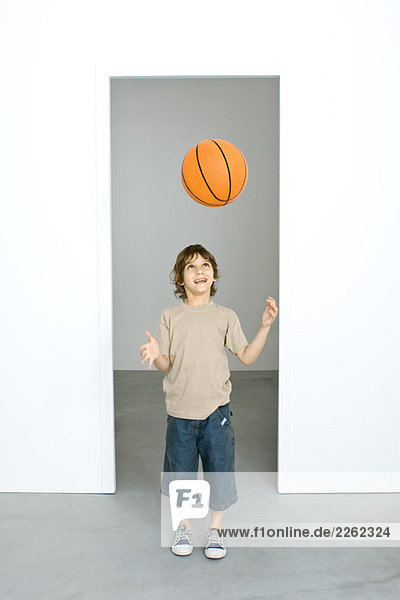 Kleiner Junge wirft Basketball in die Luft  schaut auf  lächelt.