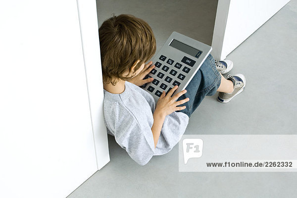 Kleiner Junge auf dem Boden sitzend  mit großem Taschenrechner spielend  hoher Blickwinkel