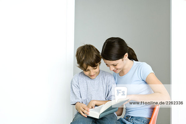 Bruder und Schwester sitzend  gemeinsam Buch lesen  beide lächelnd
