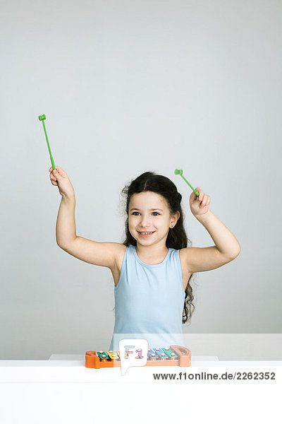 Kleines Mädchen spielt Xylophon  Arme erhoben  lächelnd