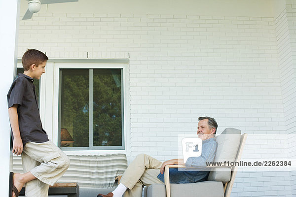 Großvater und Enkel zusammen auf der Terrasse  Junge stehend  Mann sitzend