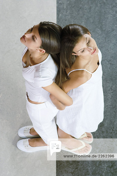 Zwillingsschwestern stehen Rücken an Rücken  Arm in Arm  von oben gesehen