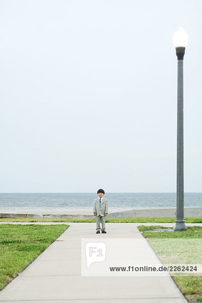 Junge in vollem Anzug  am Ende des Weges stehend  in die Kamera schauend