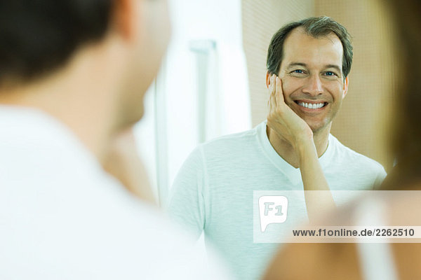 Mann mit der Hand seiner Frau auf der Wange  lächelnd bei der Reflexion im Spiegel  über die Schulter blickend