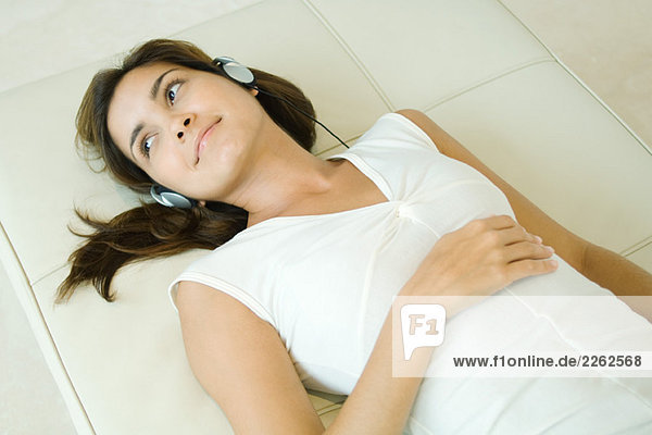Young woman lying on back listening to headphones  smiling  high angle view