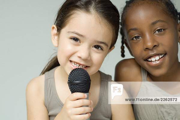 Two little girls smiling at camera together  one holding up microphone