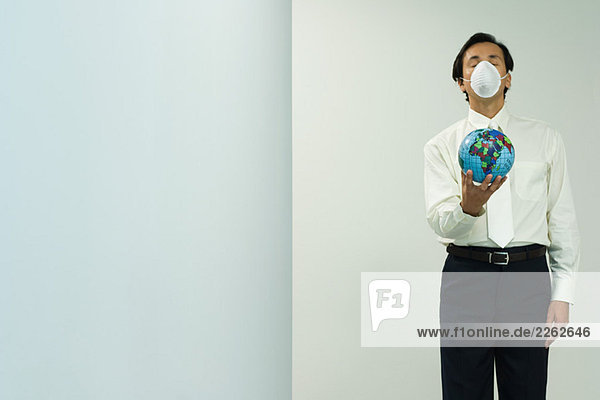 Geschäftsmann mit Verschmutzungsmaske  Globus haltend  Augen geschlossen  Frontansicht