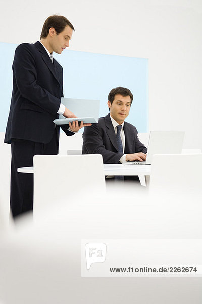 Two businessmen looking at laptop computer together  one holding folder
