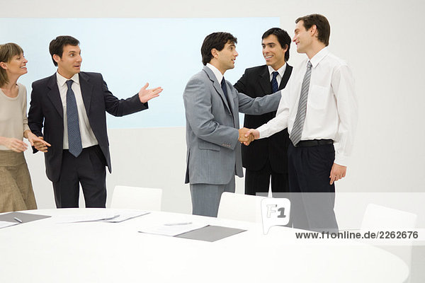 Group of professionals standing beside table  smiling  two shaking hands