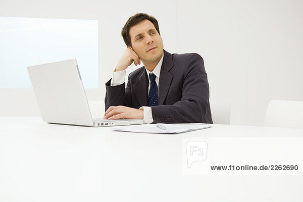 Businessman using laptop computer at desk  holding head  looking away