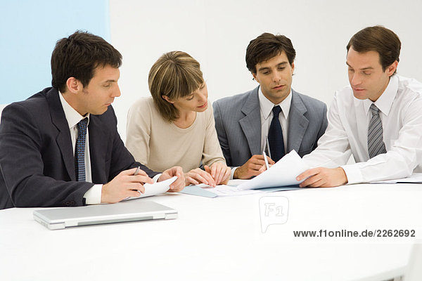 Four business partners sitting together at table  looking at document