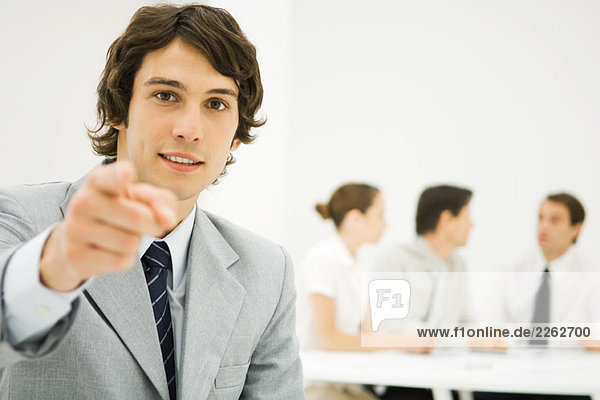 Businessman pointing at camera  personal perspective  associates in background