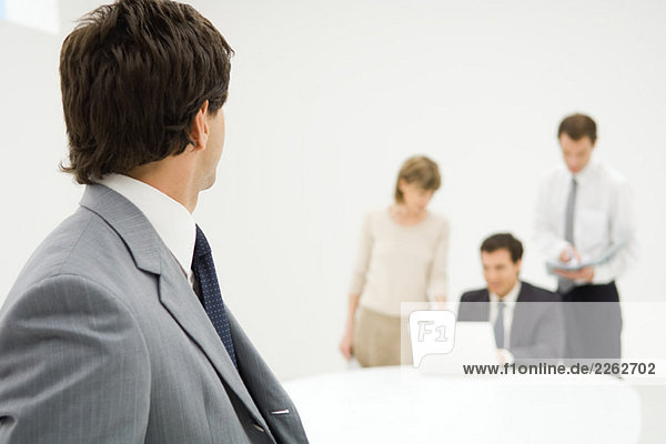 Businessman looking over shoulder at associates in background  close-up