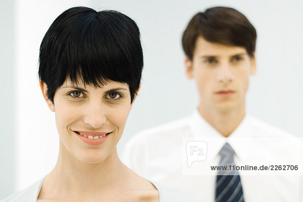 Businesswoman smiling at camera  close-up  male colleague in background