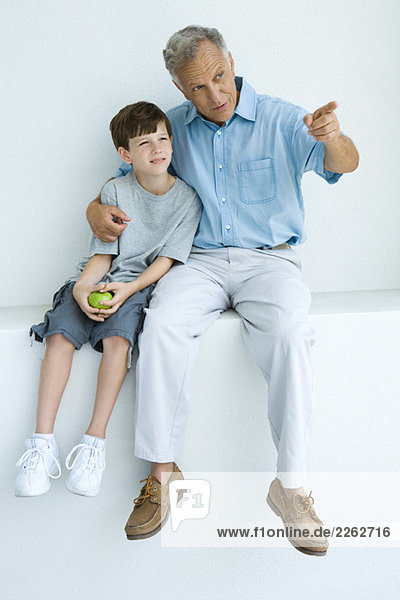 Man sitting with arm around grandson's shoulders  pointing  both looking away