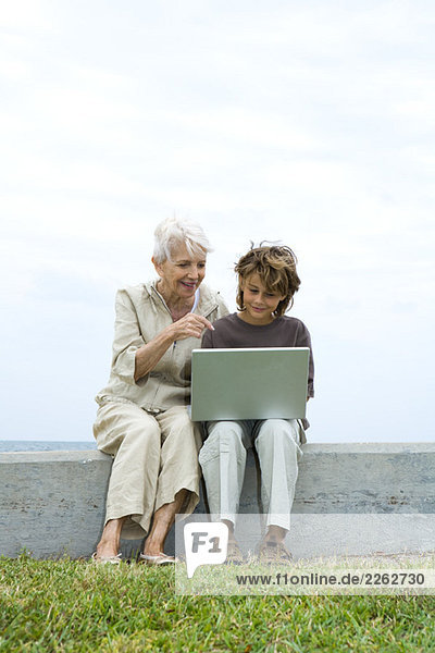 Senior Frau und Enkel sitzen im Freien  mit Laptop-Computer zusammen