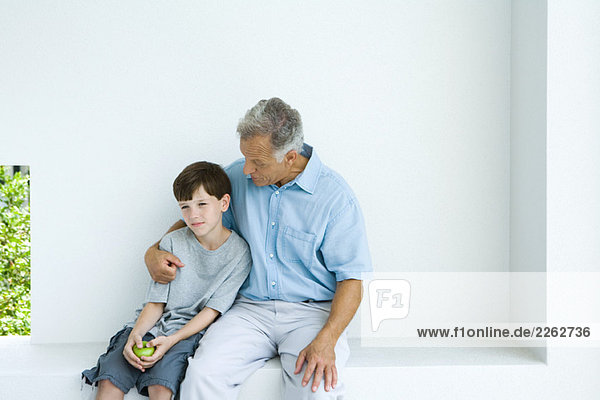 Man sitting with arm around grandson  chatting  both looking away