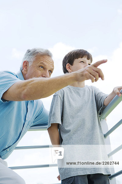 Großvater und Enkel stehen zusammen am Geländer  der Mann zeigt  beide schauen weg.