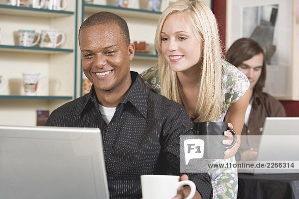 Junge Frau schaut Mann am Laptop über die Schulter