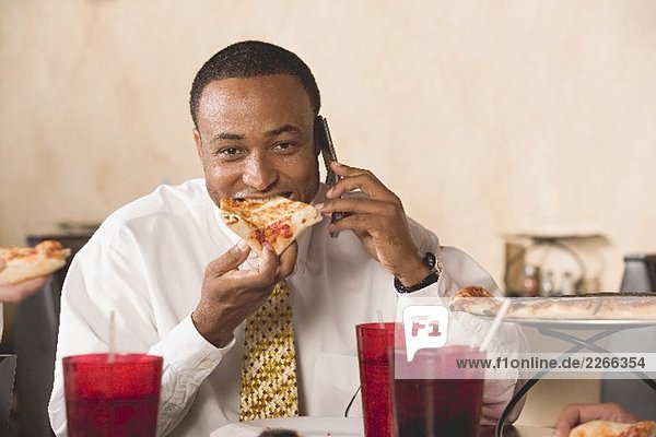 Geschäftsmann isst Pizza und telefoniert im Restaurant