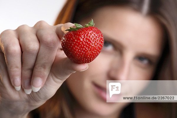 Junge Frau hält eine Erdbeere in der Hand