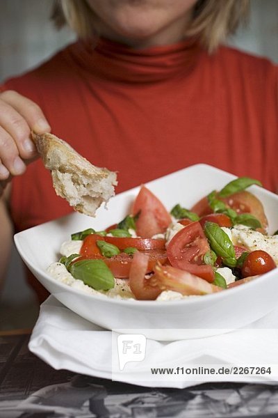 Frau isst Brot zu Tomaten mit Mozzarella und Basilikum
