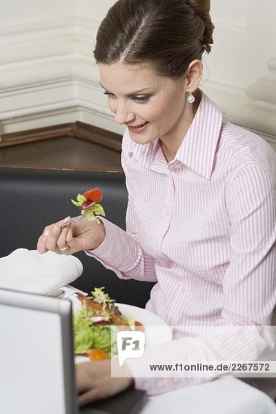 Frau isst Salat bei der Arbeit am Laptop im Restaurant