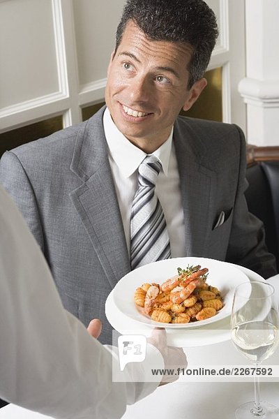 Waiter serving gnocchi with prawns to man