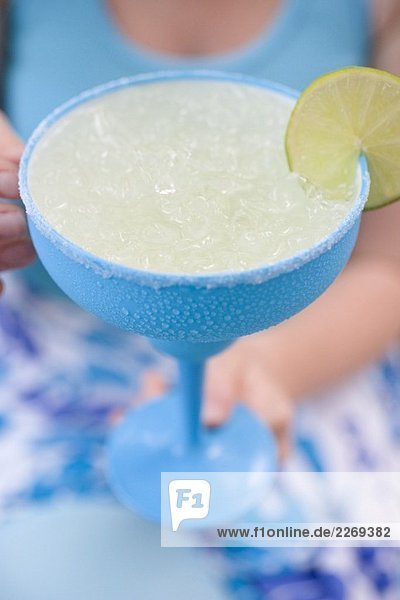 Frau hält türkisfarbenes Glas mit Limettencocktail