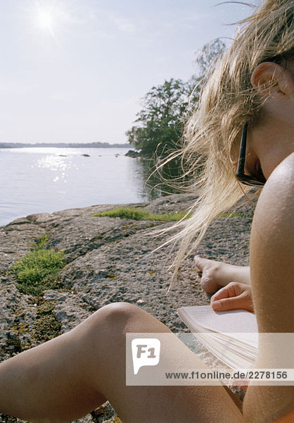Eine junge Frau beim Lesen am See