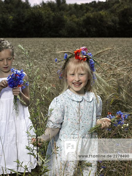 Zwei Mädchen auf einem Weizenfeld mit Trauben auf Wildblumen