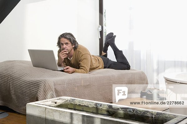 Ein Mann  der auf einem Bett liegt und einen Laptop benutzt.