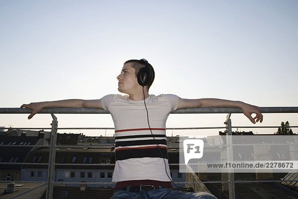 Ein junger Mann  der auf einem Dach sitzt und Kopfhörer trägt.