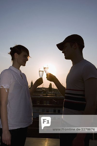 Ein junges Paar  das bei Sonnenuntergang auf einer Dachterrasse mit Champagner anstößt.